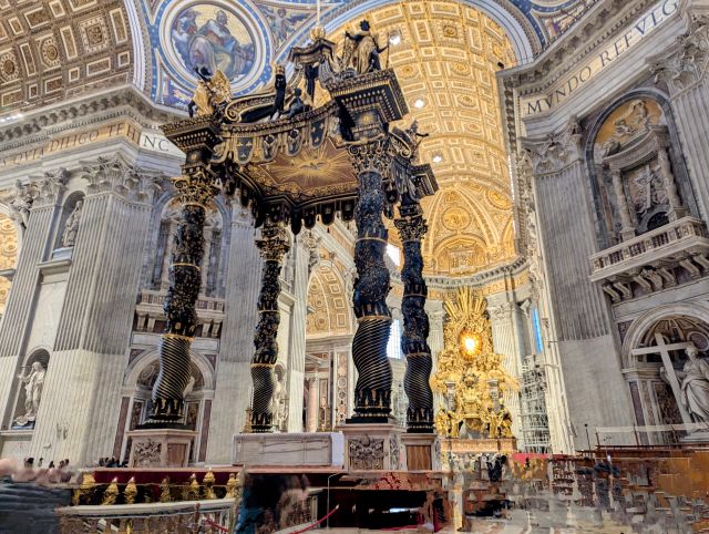 Interior of St. Peter's Basilica in Vatican City, featuring the elaborate Baroque Papal Altar and Baldachin with its twisted columns and other architectural details and artwork visible in the background.