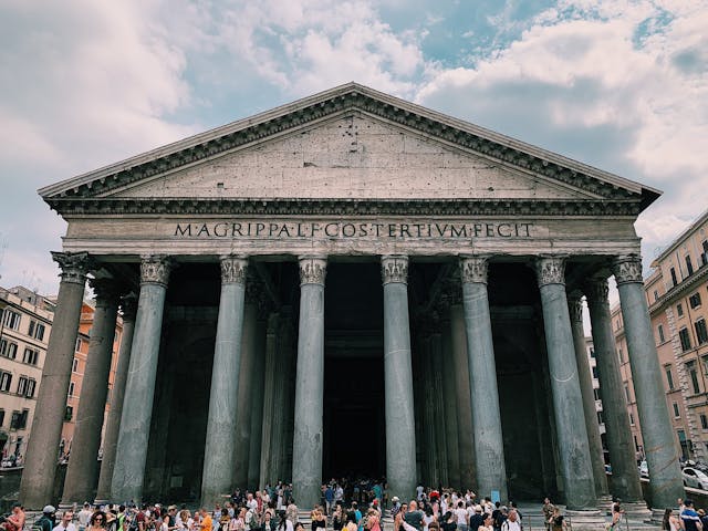 The Pantheon in Rome, Italy, a historic building with a prominent portico of granite columns, featuring an inscription on its architrave, under a cloudy sky.