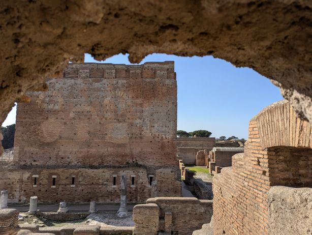 Ruins of Ostia Antica, the ancient port of Rome, in Italy, featuring a large, well-preserved tower on the left, constructed of brick, and other remains of buildings with similar construction techniques visible in the background, under a clear blue sky.