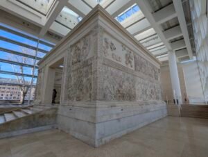 Ara Pacis-alteret set fra hjørnet, med processionsfrisen ovenover og de vegetabilske spiraldekorationer nedenunder, inde i sin beskyttende museumsbygning