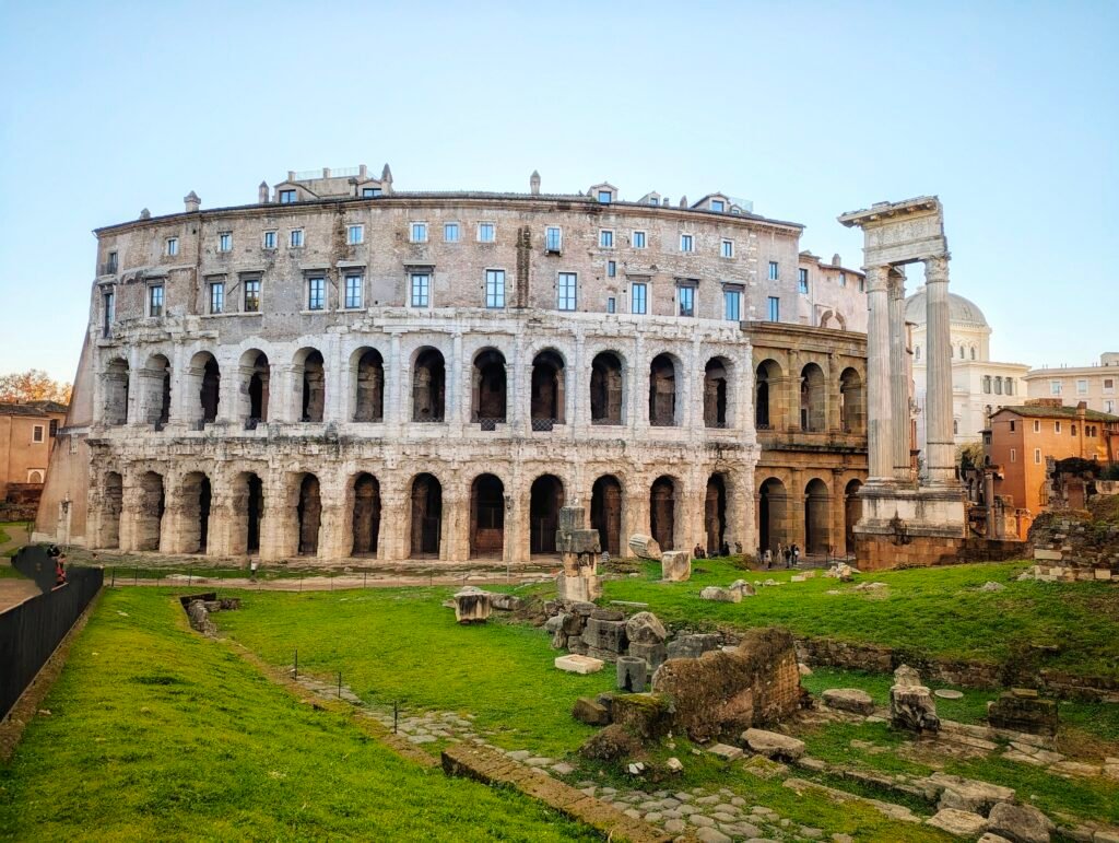 Udsigt over det antikke Marcellus-teater i Rom, der viser dets historiske buer i etager og de tilstødende søjler fra Apollon Sosianus-templet.