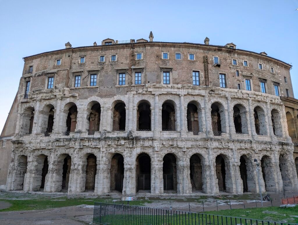Frontudsigt over det historiske Marcellus-teater i Rom, der viser dets gamle stenbuer og den senere renæssanceboligstruktur bygget på toppen.