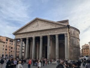 Fuld frontudsigt over det gamle Pantheon i Rom, der viser dets ikoniske portik, granitsøjler og historiske inskription under en blå himmel.