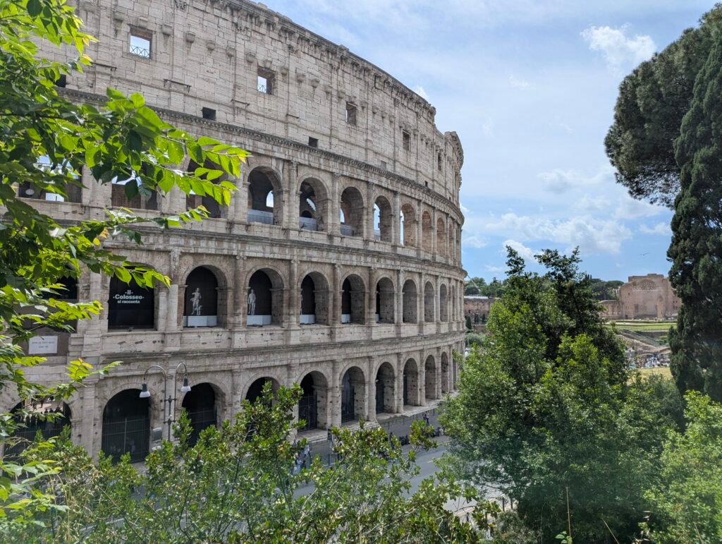 View of the Colosseum's arched facade through green summer foliage in Rome