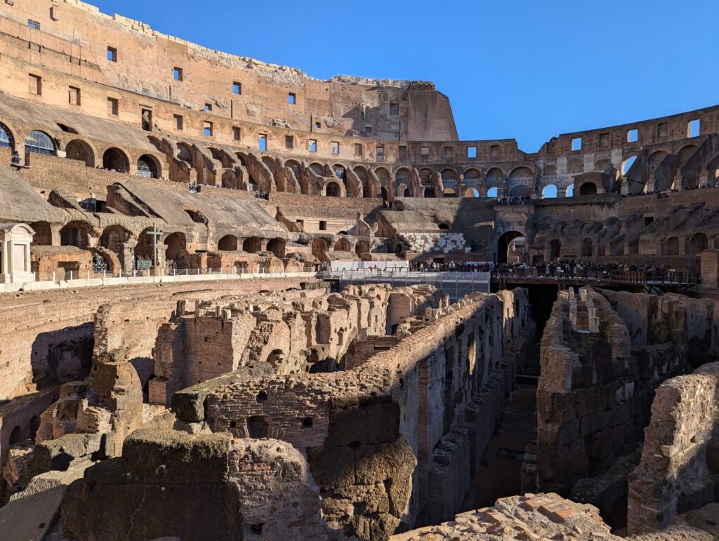 View of the Colosseum's hypogeum and upper tiers, with a memorial cross visible on the left