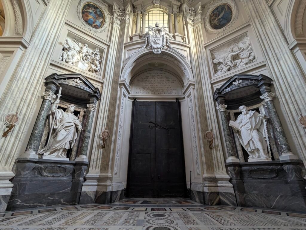 Lavvinkel innvendig utsikt over den monumentale døren, marmorstatuer, relieffskulpturer og det utsmykkede kassetttaket inne i San Giovanni in Laterano-basilikaen i Roma.