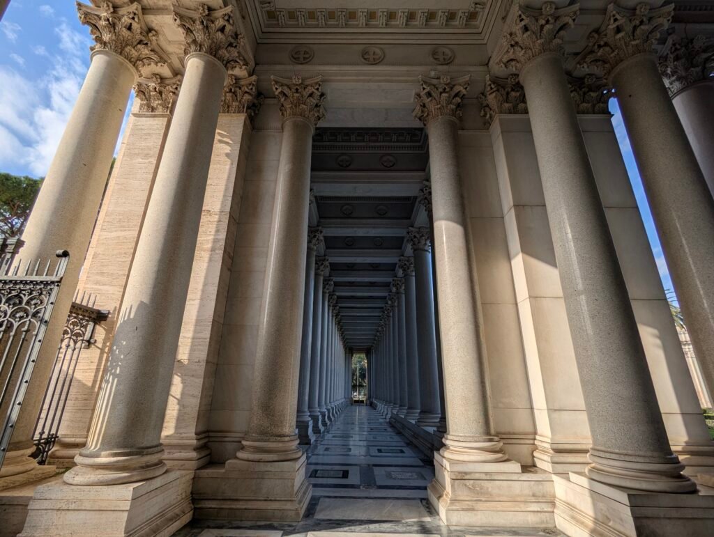 Perspektivutsikt nedover en lang, elegant søylegang med klassiske korintiske søyler og marmorgulv ved basilikaen San Paolo fuori le mura i Roma.