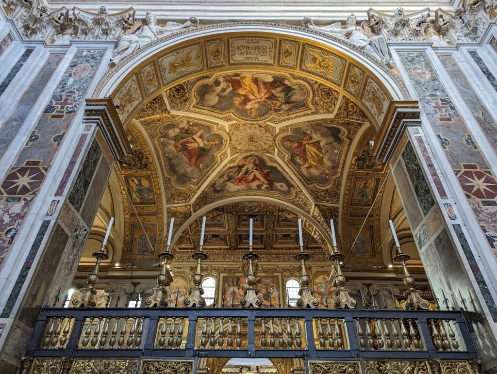 Lavvinkelutsikt over det rikt forgylte hvelvtaket utsmykket med religiøse fresker, gullfargede kandelabere og intrikate rekkverk i marmor og jern inne i den pavelige basilikaen Santa Maria Maggiore i Roma.