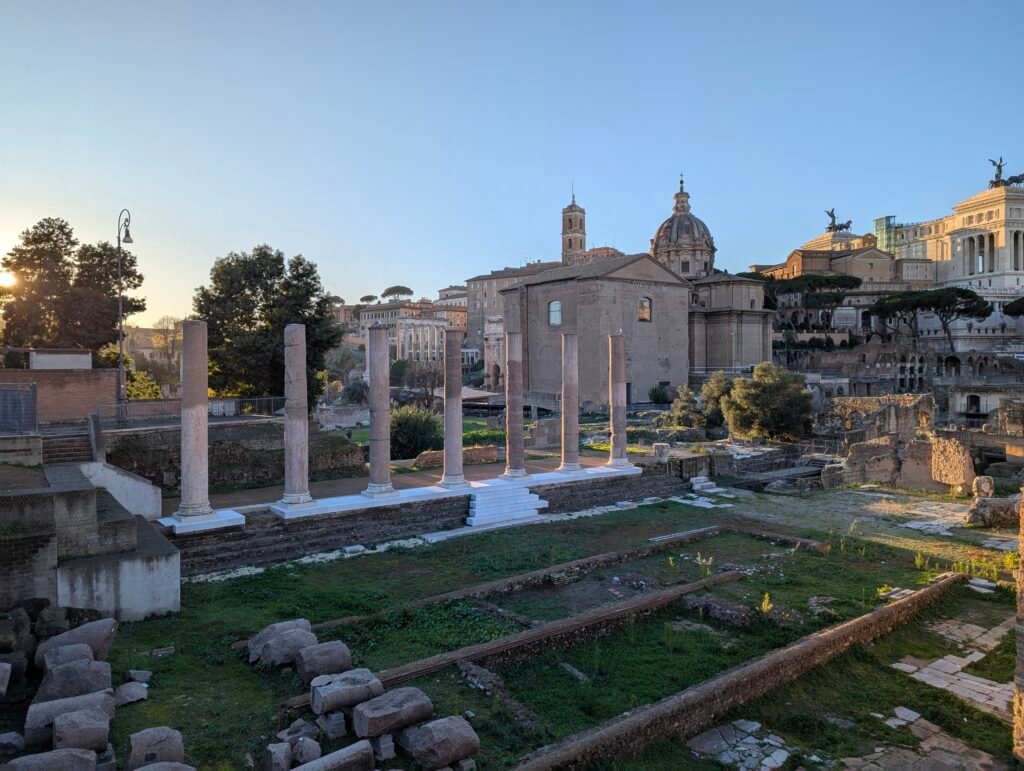 Rad av antika marmorpelare i Forum Romanum vid solnedgången, med Roms skyline i bakgrunden