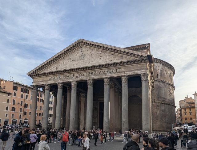 Fullständig frontvy över det gamla Pantheon i Rom, som visar dess ikoniska portik, granitpelare och historiska inskription under en blå himmel.
