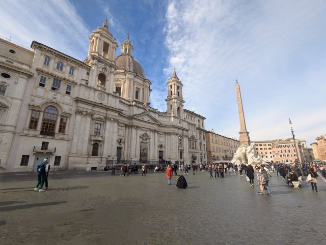 Brett perspektiv av Piazza Navona i Rom med Berninis Fontana dei Quattro Fiumi, den centrala obelisken och kyrkan Sant'Agnese in Agone under en delvis molnig himmel.