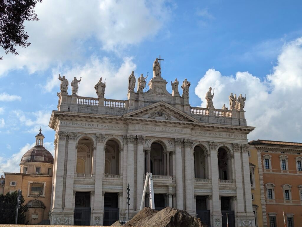 Imponerande fasad av San Giovanni in Laterano-basilikan i Rom, med statyerna av Kristus och apostlarna under en blå himmel.